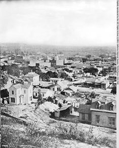 an old black and white photo of a city from the top of a hill with buildings