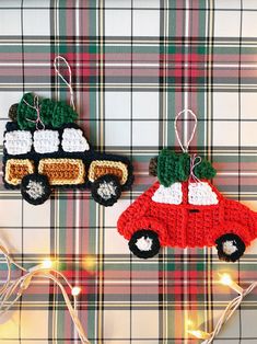 two crocheted christmas ornaments hanging on a plaid tablecloth with lights in the background