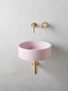 a pink sink with gold faucet on the wall next to it and a round mirror