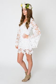 a woman wearing a white dress with flowers in her hair is posing for the camera