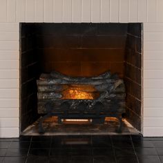 a fire place with logs in it and tiled flooring on the side, next to a white brick wall