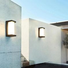 two lights on the side of a white wall next to a potted plant and stairs