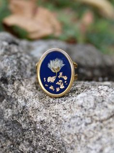 Floral ring, Baby's breath flower on deep blue background and gold leaves. Adjustable gold stainless steel ring. Cabochon: 21 x 16 mm (0.8 x 0.6 inch)  This ring is the perfect accessory for women who love minimalist dainty jewelry. It makes a thoughtful and stylish gift for any occasion, whether it's for Mother's Day, a birthday, or as a treat for yourself ! 🎁 -- ✨CUSTOM ORDER: We're happy to create custom orders to suit your unique style and preferences. Need a different length or color for your jewelry? Just send us a message with your request and we'll work with you to make it happen!  🌼INFORMATIONS:  *Gift wrapping option available. *Handmade with care in Dordogne, France ✍️Where to find us? *Instagram: www.instagram.com/paquerettepaillette/ *Mail: paquerettepaillette@gmail.com Dainty Jewelry Gold, Dried Flower Jewelry, Jewelry Dainty, Floral Ring, Gold Leaves, Baby's Breath, Jewelry Boho, Flower Jewelry, Ring Women