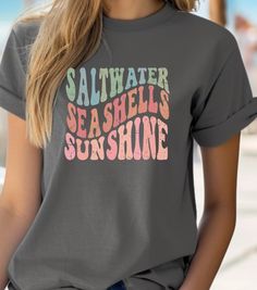 This Tee exudes a coastal vibe with its Saltwater, Seashells, Sunshine design, perfect for those who love the beach and summer. It is a versatile piece that can be worn casually or layered for a more stylish look. Ideal for beachgoers, summer lovers, and those who enjoy the laid-back lifestyle. Perfect for vacations, beach days, and outdoor gatherings. Product features - Ribbed knit collar for elasticity - Made from smooth, strong fabric - Medium fabric for year-round comfort - Ethically and sustainably made - Plus Sizes Available - Sizes: S-5XL - More Colors and Kids Sizes Available - Message Me If You're Interested  Care instructions - Machine wash: warm  - Non-chlorine: bleach as needed - Tumble dry: medium - Do not iron - Do not dryclean Sunshine Shirt, Beach Tee, Vacation Tops, Coastal Vibes, Simple Joys, Summer Gifts, Ocean Lover, Casual Summer Shirts, Summer Tee