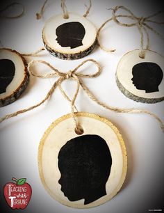 three ornaments with black silhouettes on them hanging from twine strings and tied to wood slices