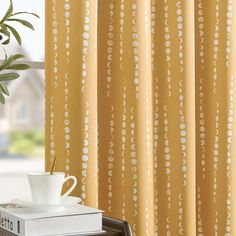 a coffee cup sitting on top of a stack of books next to a window curtain