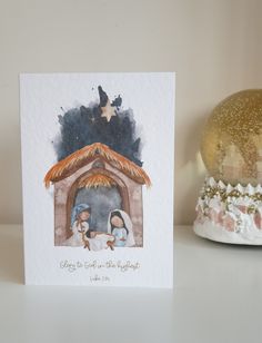 a christmas card with a nativity scene on it next to a snow globe and an ornament