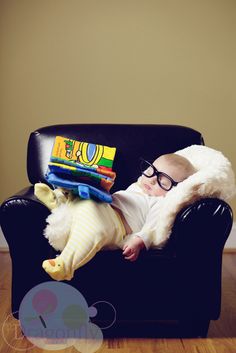 a baby wearing glasses is laying on a black chair with a book in it's lap