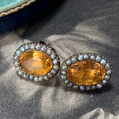 Georgian topaz and split pearl earrings in a closed back gold setting. A stunning pair of earrings beset with a split natural pearl halo that surrounds a majestic oval cut topaz. In outstanding condition, circa 1800 - 1820 and historically converted to post and butterfly fittings for easy and everyday use. Very rare indeed especially in this amazing condition. A very splendid and truly mesmerizing antique treasure to grace your ears. In historical contexts, topaz was considered a protective ston Pearl Halo, Antique Boxes, Natural Pearl, Natural Pearls, Jewelry Earrings Studs, Oval Cut, Very Rare, Bridal Jewelry, Favorite Jewelry