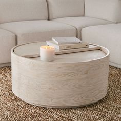 a coffee table with a candle and books on it in front of a white couch