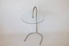 a round glass table with metal legs on a white background, against a plain wall