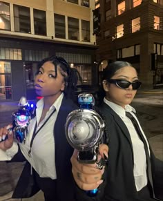 two women dressed in black and white are holding some lights on their hands as they stand outside at night