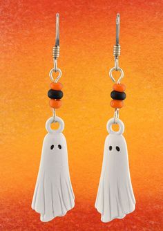 two white ghost earrings with black beads hanging from hooks on an orange and yellow background