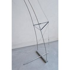 a metal sculpture on top of a cement floor next to a white wall with a wire hanging from it's side