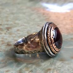 It's got to be This is a stunning ring. The band is slightly hammered. The bezel is made from yellow gold set with a deep red garnet. Garnet is a hard, brilliant stone. It occurs in certain shades of red that have been taken for some varieties of ruby. (R2432). © 2011 - 2016 Artisanimpact Inc. All rights reserved. Construction & Dimensions: Sterling silver, yellow gold, garnet. Approximate width: 16mm (0.68in). We can make any size, including quarter sizes. For this wider band, we suggest ad Unique Rings With Polished Round Band, Unique Rings With Polished Finish And Round Band, Unique Dome Ring With Polished Finish For Promise, Unique Dome Promise Ring With Polished Finish, Timeless Jewelry With Large Stone, Timeless Jewelry Ring With Large Stone, Formal Garnet Ring With Polished Finish, Timeless Large Stone Ring Jewelry, Formal Dome Ring With Open Ring Gemstone