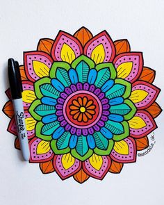 a drawing of a colorful flower on a white surface with marker pens in front of it