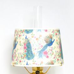 a lamp with a peacock print shade on the bottom and a gold base, sitting against a white wall