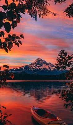 a boat sitting on top of a lake next to a tree covered shore under a colorful sky