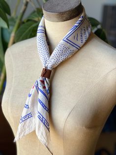 a white and blue scarf on top of a mannequin's head with a plant in the background