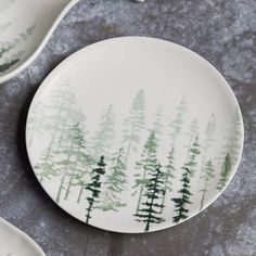 two plates with trees painted on them sitting on a table next to forks and spoons