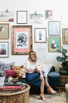 a woman sitting on top of a couch in front of a wall covered with pictures