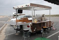 a food truck parked in a parking lot next to a white van with an awning