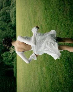 a woman in a white dress is standing on the grass with her legs spread out