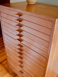 a close up of a wooden dresser on a hard wood floor with a vase in the background