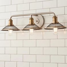 three light bathroom fixture with white tiles on the wall behind it and an old - fashioned brass finish