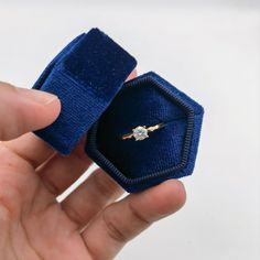 a hand holding an open ring with a diamond in it's center and blue velvet band