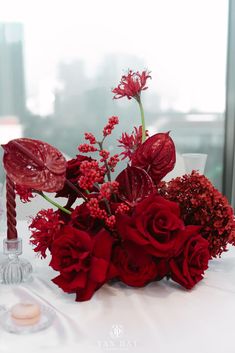 a bouquet of red flowers sitting on top of a table next to a candle holder