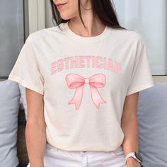 a woman sitting on a couch wearing a tee shirt with a pink bow at the front