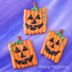 three decorated halloween cookies sitting on top of a purple cloth covered table with blue background