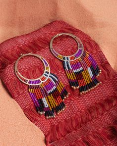 These handmade beaded earrings feature premium Japanese glass Miyuki beads which are woven onto a stunning brass earring component. Inspired by the beautiful colors found in the deserts of the Southwest, these statement earrings combine a bold geometric design with accents of black and white for contrast. Each strand of hand strung fringe is adorned with a tubular and a gold drop bead. The brass component is attached to a stainless steel ball post. These earrings are handmade by women artisans i Artisan Multicolor Beaded Earrings With Gold Beads, Handwoven Bohemian Festive Jewelry, Bohemian Handwoven Festive Jewelry, Festive Handwoven Bohemian Jewelry, Festive Bohemian Handwoven Jewelry, Traditional Multicolor Beaded Earrings With Gold Beads, Bohemian Beaded Earrings With Colorful Beads, Woven Dangle Earrings For Festival, Bohemian Woven Dangle Beaded Earrings