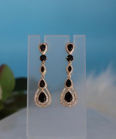 These earrings boast a bold pear-shaped design, embellished with deep black cubic zirconia (CZ) stones that offer a striking contrast. The dangling construction allows them to swing gracefully with every movement, adding a sophisticated and edgy flair to any ensemble. Length: 2 inches Width: 0.50 inches Closure: Bullet with Disc Backs Material: Brass with 18K Gold Plating with Rhodium Coating Lead Free and Hypoallergenic Evening Teardrop Chandelier Earrings With Sparkling Stones, Glamorous Black Jewelry With Sparkling Stones, Evening Pear-shaped Cubic Zirconia Earrings, Formal Earrings With Black Diamonds And Cubic Zirconia, Formal Cubic Zirconia Earrings With Black Diamonds, Formal Black Diamond Cubic Zirconia Earrings, Evening Teardrop Earrings With Sparkling Stones, Pear-shaped Earrings For Party With Pierced Ears, Sparkling Drop Teardrop Earrings For Evening