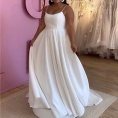 a woman standing in front of a pink wall wearing a white dress and large earrings