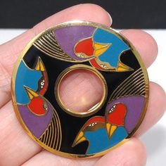 "*Description: This is a great Laurel Burch \"Birds of Santorini\" circular brooch with a cloisonne gold plated design of six birds in bright enamel colors of teal blue, purple, red, and orange, on a black enamel background from the 1980s. The doughnut shaped design is stamped Laurel Burch and Birds of Santorini on the back with a rolling C clasp. This would be a great addition to your vintage jewelry collection or make a great vintage gift! This amazing artist, Laurel Burch, is known for her co Unique Collectible Brooch, Vintage Round Enamel Pin For Gift, Laurel Burch, Small Pin, Red And Orange, Cloisonne Enamel, Plate Design, Enamel Jewelry, Single Earring