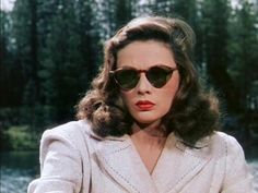 an old photo of a woman wearing sunglasses and a coat with trees in the background