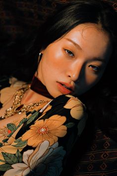 a woman wearing a floral shirt and necklace laying on a couch with her eyes closed