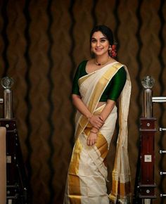 a woman in a white and green sari standing next to a wooden stand with a vase on it