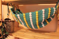 a crocheted bag hanging from a shelf next to a potted plant on a wooden shelf