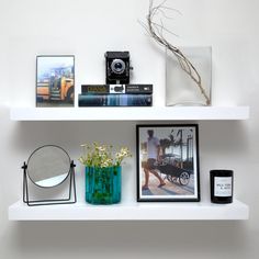 a white shelf with pictures, flowers and other items on it next to a mirror