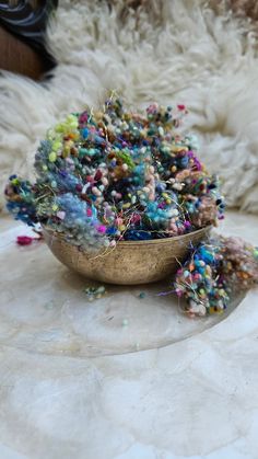 a bowl filled with lots of beads on top of a white rug next to a pile of fur