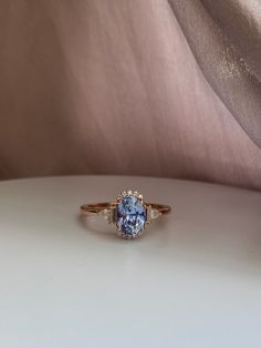 a blue diamond ring sitting on top of a white table next to a pink cloth