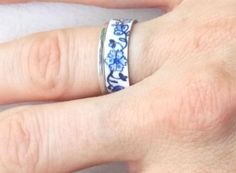 This ring is inspired by antique Delftware from Holland. The deep blue floral design on a white background is timeless and versatile, blending well with outfits from jeans through sundresses. The classic, beloved blue/white color combination looks great on any skin tone. This is a detailed, unique ring that is sure to be noticed! My original hand drawn and painted design is dyed and heat sealed by me on this aluminum ring. It is extremely durable; the process allows the colors to become part of Blue Flower Ring For Gift, Unique Blue Flower Ring For Gift, Blue Sterling Silver Promise Flower Ring, Blue Sterling Silver Promise Ring, Vintage Blue Enamel Ring For Gift, Handmade Blue Flower Ring For Anniversary, Handmade Blue Open Ring Jewelry, Handmade Blue Promise Ring, Elegant Blue Adjustable Flower Ring