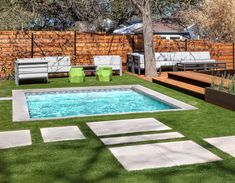 a backyard with artificial grass and pool surrounded by wooden fenced in seating area, green lawn chairs and white couches