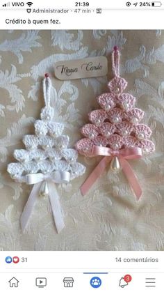 two crocheted christmas tree ornaments on a white and pink bed sheet with ribbon