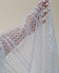 a woman's hand is holding up a white lace curtain with circles on it