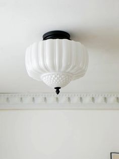 a white light fixture hanging from the ceiling above a bed in a room with white walls