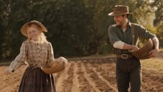 a man and woman walking down a dirt road in the middle of a farm field